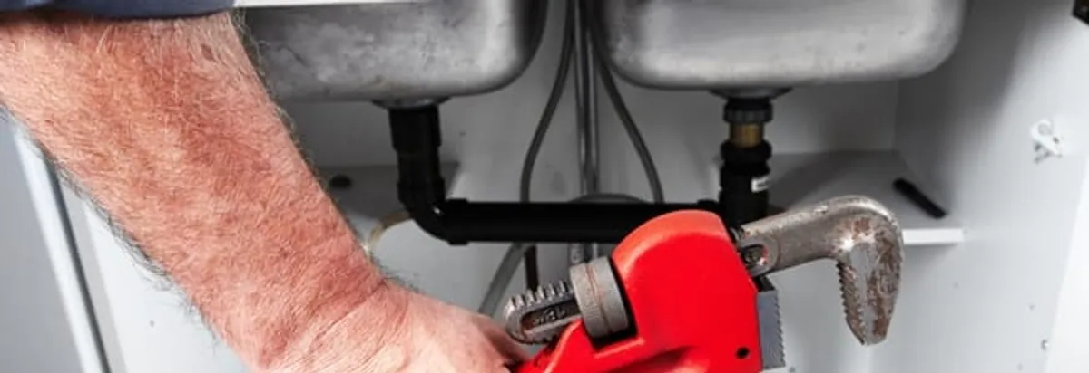 Garbage disposal repair technician tightening drain connections under a kitchen sink in Arvada, CO