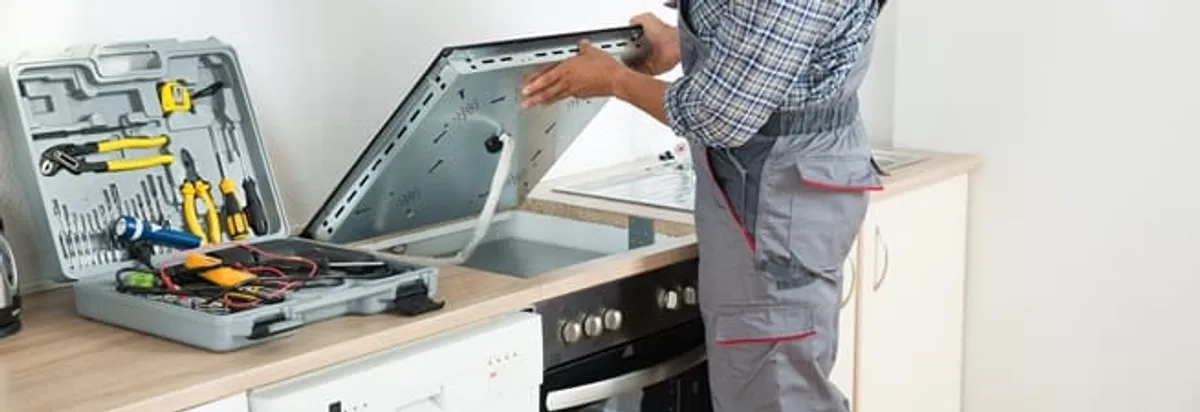 Cooktop repair technician lifting a built-in stovetop for service in Arvada, CO