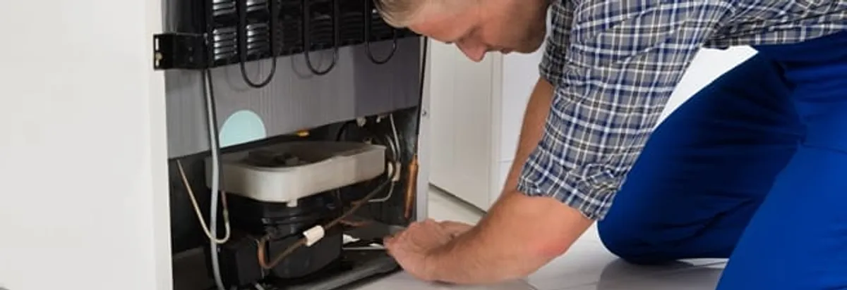 Refrigerator repair technician servicing the compressor and condenser area in Arvada, CO